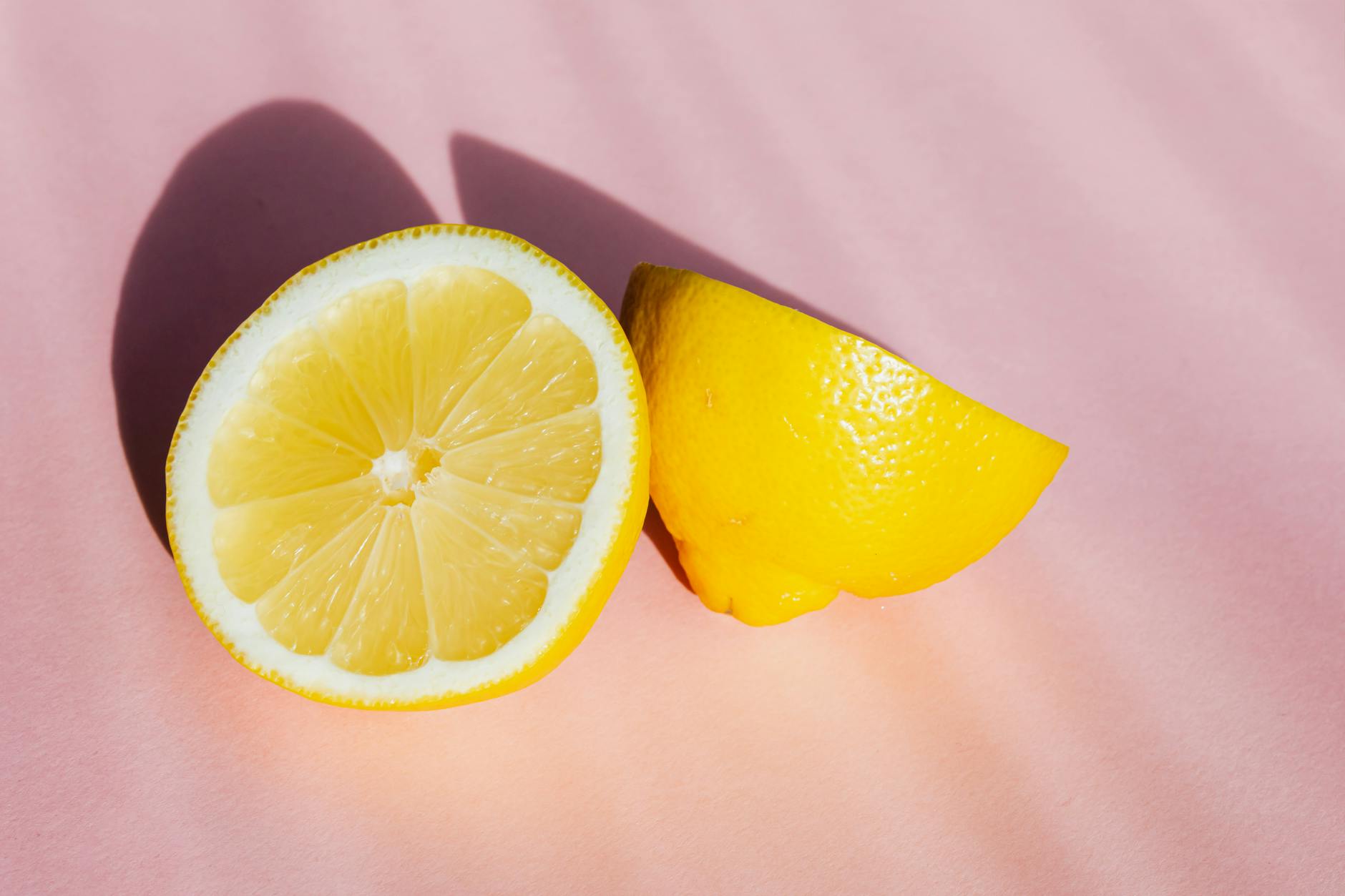 Sliced lemon halves on a pink background with natural sunlight, symbolizing the bright intensity options of a lemon vibrator