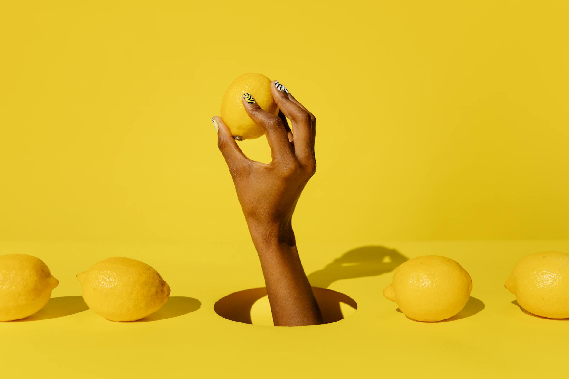 Hand holding a fresh lemon against a vivid yellow background, symbolizing natural, unhurried pleasure